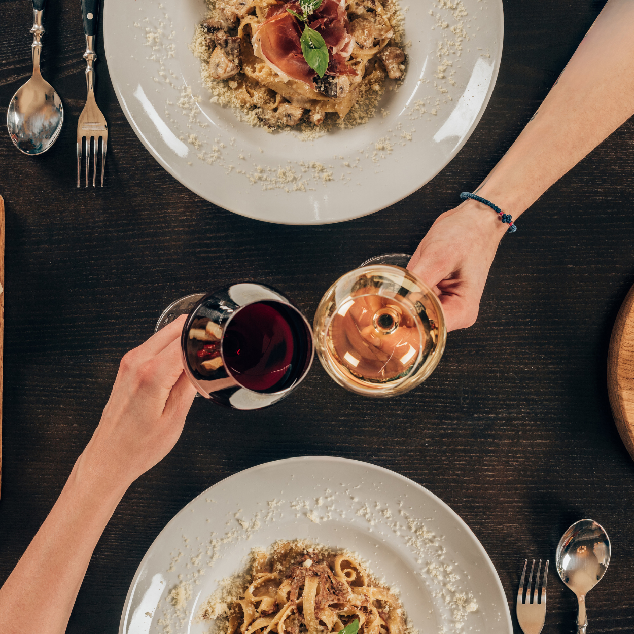 Two hands holding wine glasses with pasta dinner entrees