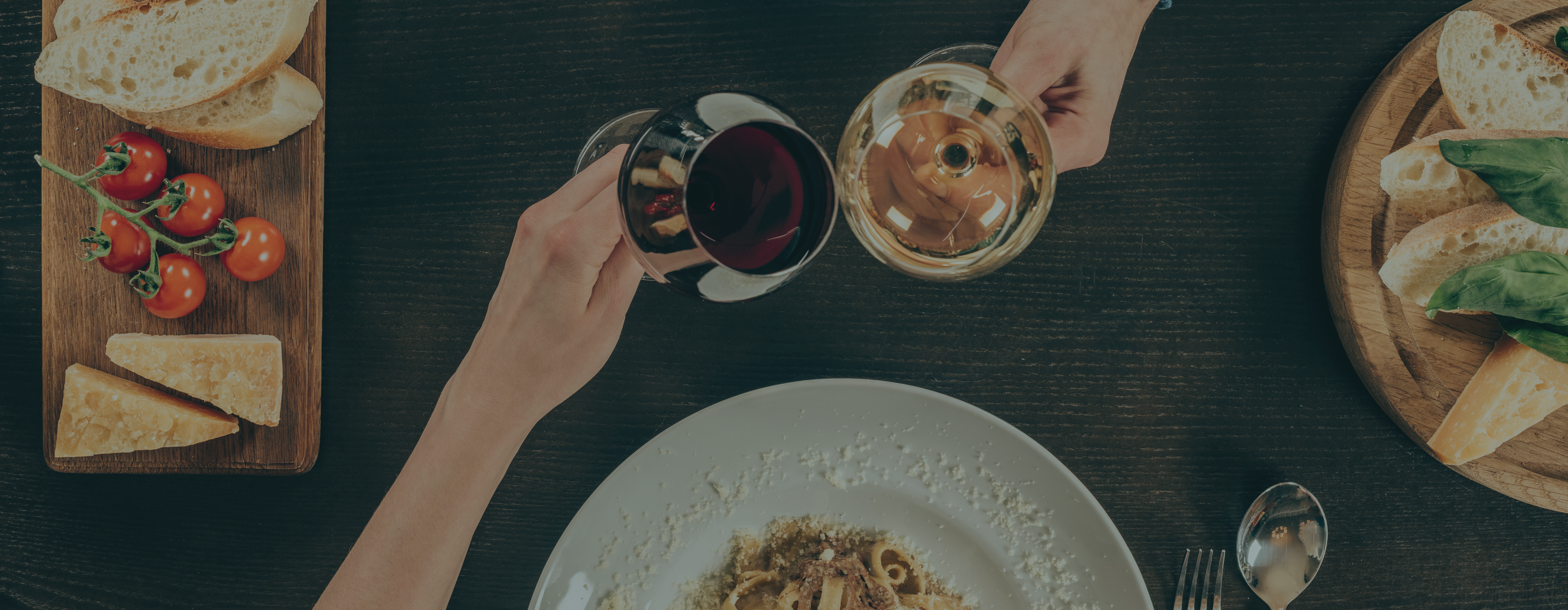 Overhead view of dinner table featuring two hands holding wine glasses and appetizers